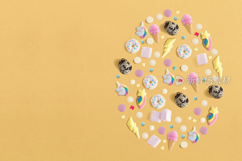 布置装饰为快乐复活节，节日背景概念。彩色的鸡蛋，糖果和装饰设计，如大鸡蛋黄色蜡笔书桌与复制空间。平躺