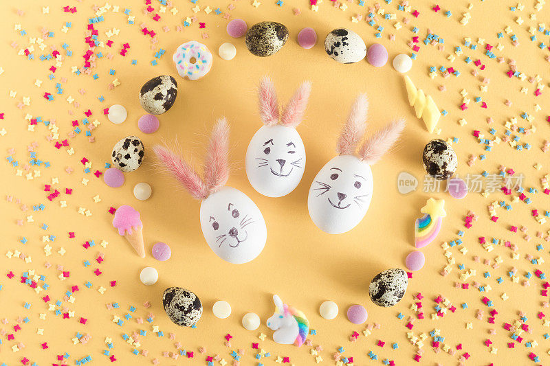 复活节餐桌上的糖果和彩蛋。彩蛋与复活节兔子耳朵在黄色背景，俯视图拷贝空间