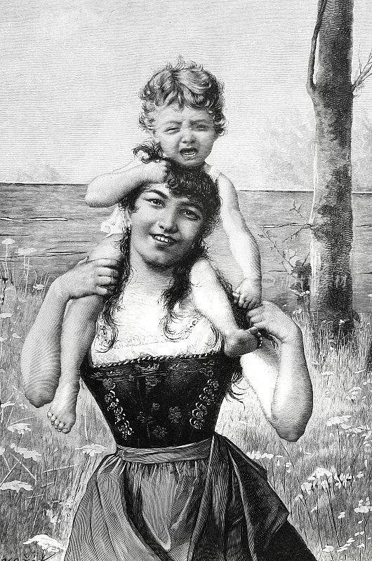 年轻的母亲背着她的孩子在花草地上