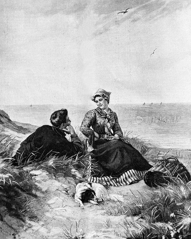 一对年轻夫妇带着狗坐在海边的小山上聊天