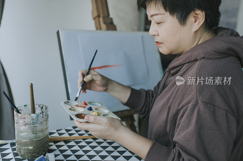 一位亚洲华裔女艺术家在家里用她的调色板、画笔和画纸在画架上画画