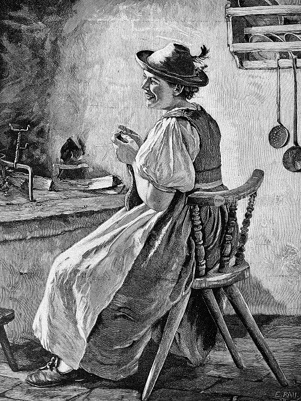 快乐的年轻巴伐利亚妇女坐在厨房的椅子上，编织和愉快地与某人交谈，侧视图