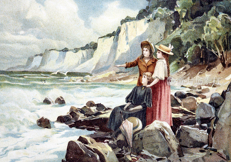 三个女孩在海滩上，站着坐着，在岩石之间望着大海