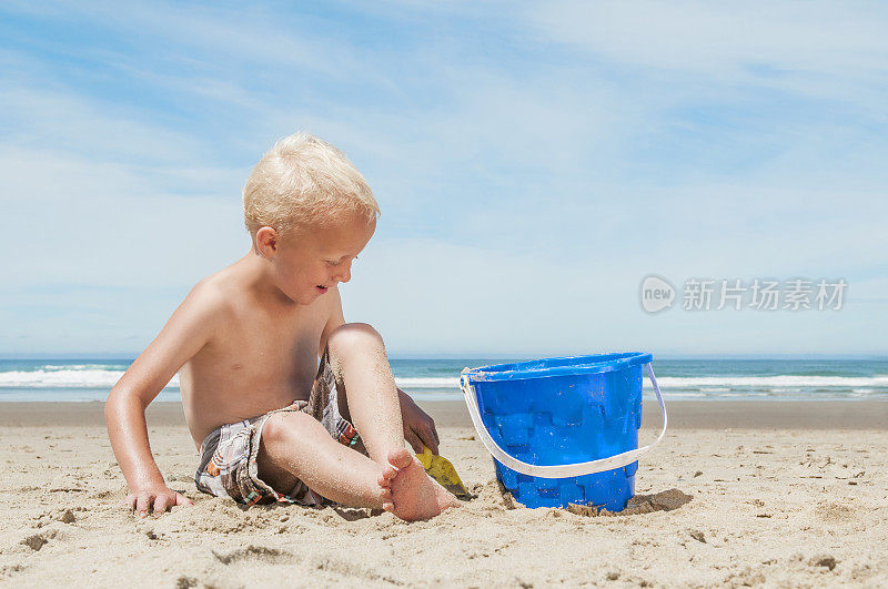 小男孩在沙滩上玩水桶。