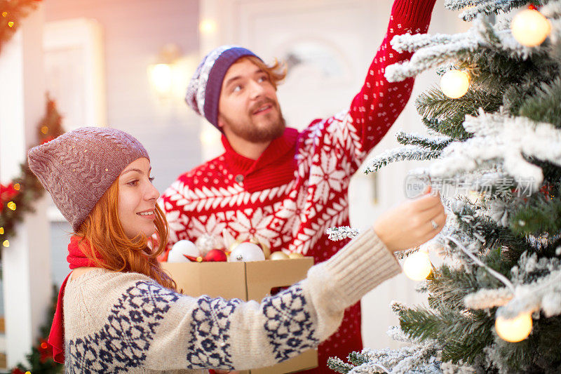 一对夫妇在房子前装饰圣诞树。