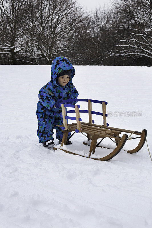 微笑的蹒跚学步的孩子在雪地里推着雪橇