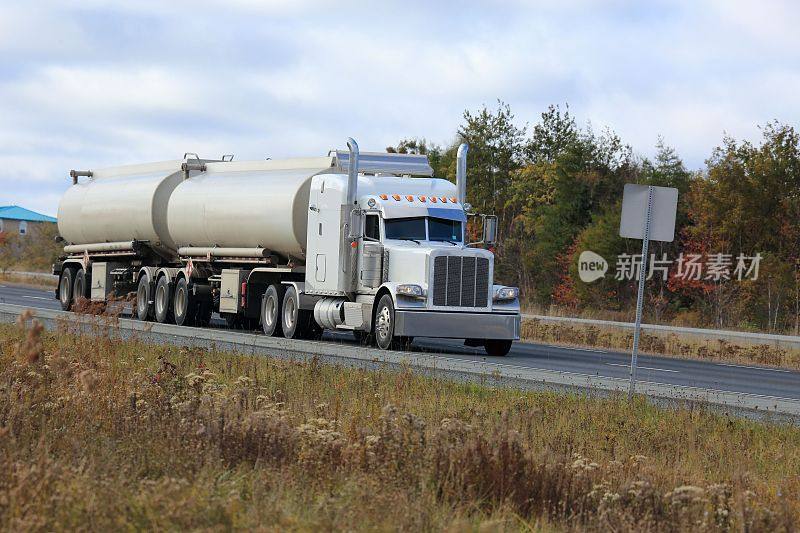 公路上开着半油罐车，后面是树。