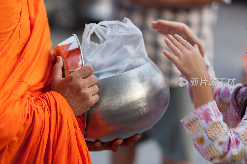 一个泰国佛教僧侣接受一个年轻的外行的施舍，他刚刚把食物放进曼谷一个泰国佛教寺庙外的和尚的施舍碗里。