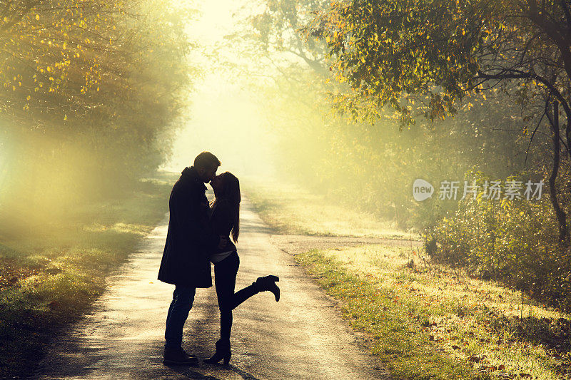 一对年轻的情侣在秋天的阳光下接吻