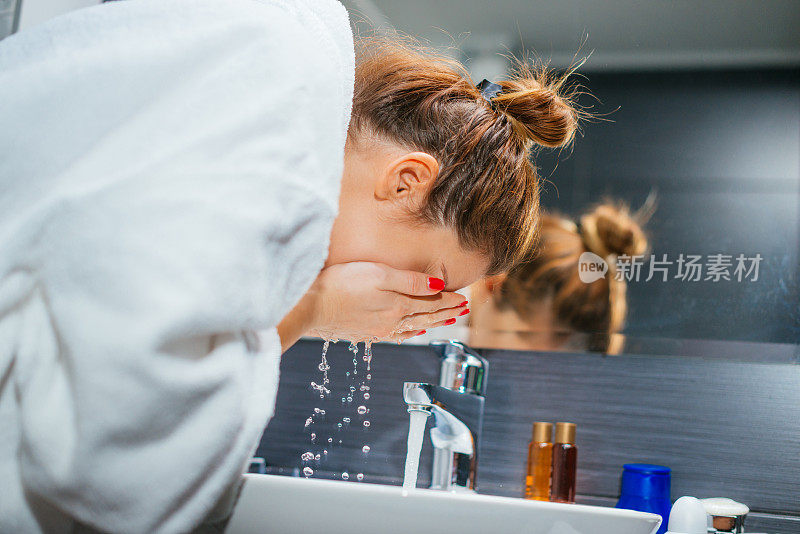 一个穿着浴袍的女人在浴室里洗脸