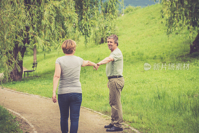 一对老年白种夫妇在户外散步，手牵着手，回头看