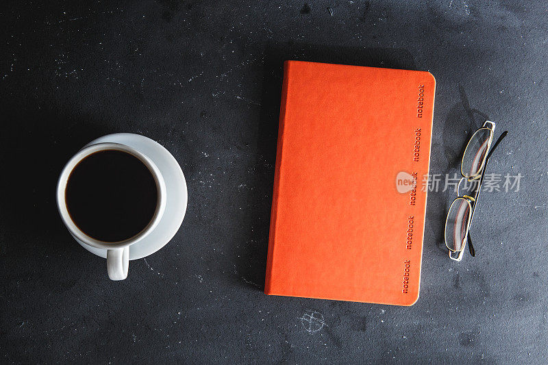 咖啡杯，笔记本，眼镜都放在黑色的桌子上