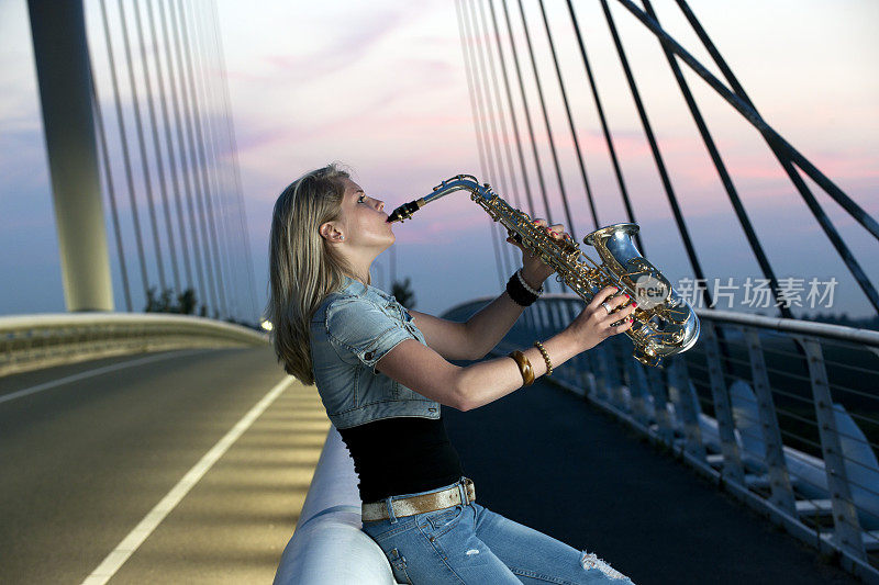 一个年轻女子在照亮的桥XXXL上吹萨克斯