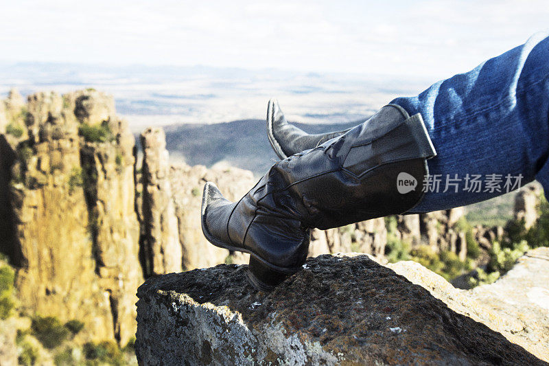 女人穿着黑色牛仔靴站在悬崖顶上
