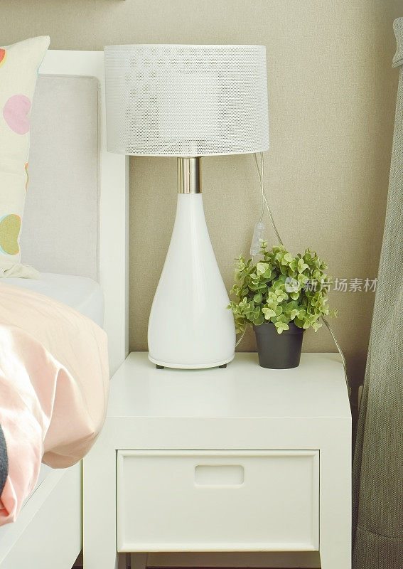 床边的桌上放着白色的灯和花盆