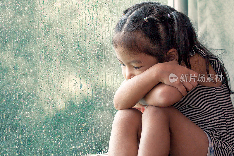 悲伤的亚洲小女孩望着窗外在雨天