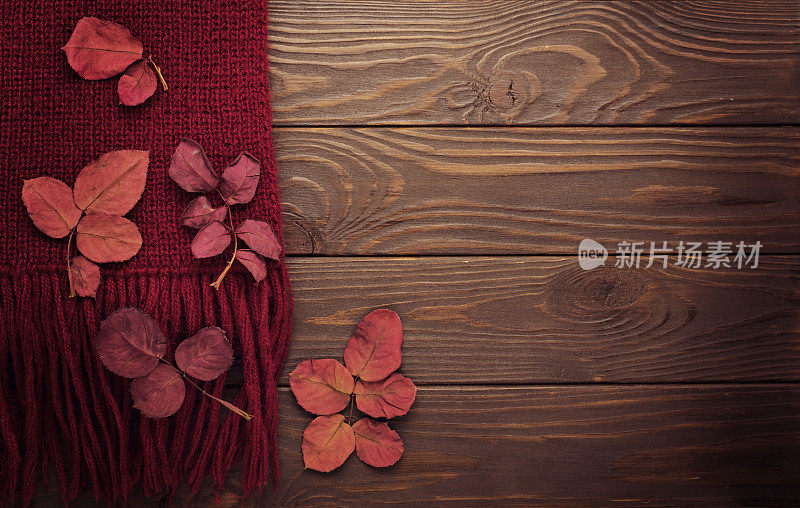编织围巾的紫红色与秋天的叶子在一个黑暗的木制背景。