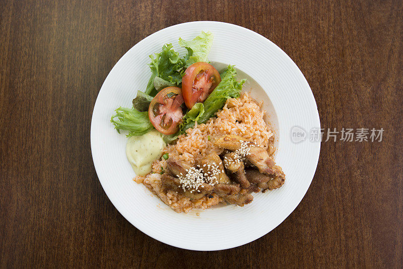 木桌上的白盘土豆鸡和蔬菜炒饭。亚洲炒饭。