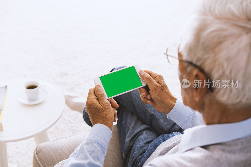坐在沙发上用绿屏智能手机的老人