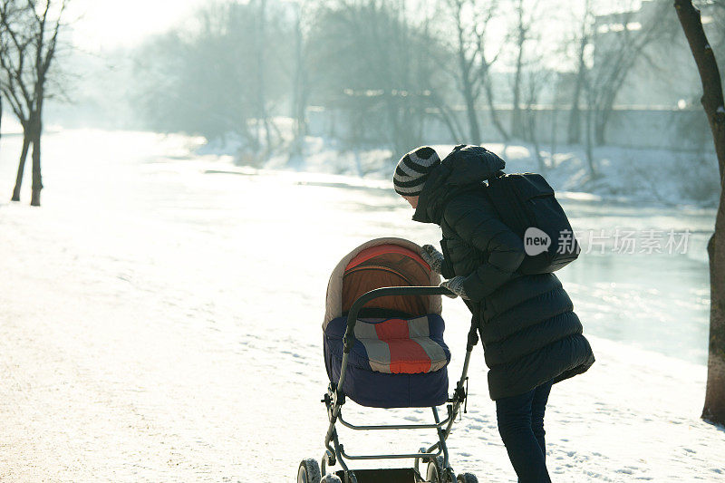一个女人推着婴儿车在冬天的公园散步