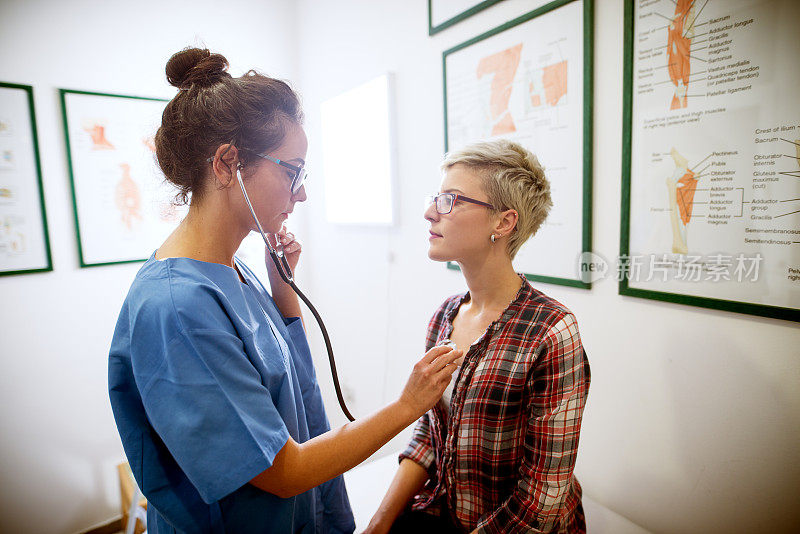 专业护士在医院办公室用听诊器检查中年短发女性患者健康状况的近侧视图。