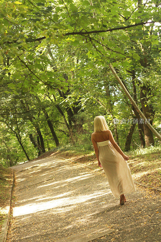 迷人的年轻女孩穿着白色的裙子走在树林里