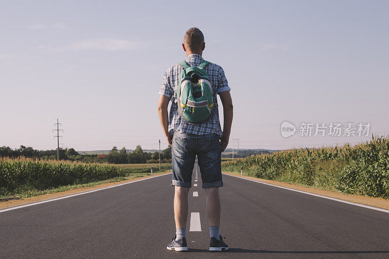 快乐的成人徒步旅行者背包徒步在柏油路在日落。后面的观点。