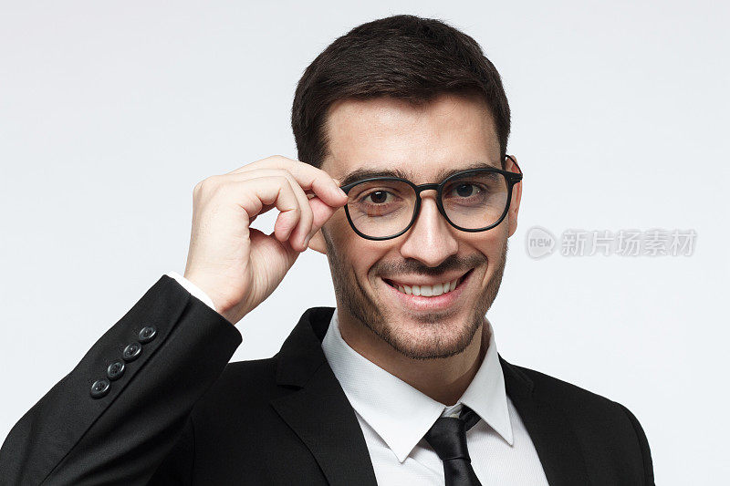 年轻的欧洲白人男性在正式服装的头像照片孤立在灰色背景拿着眼镜边缘与手指微笑友好，似乎显示关注和兴趣