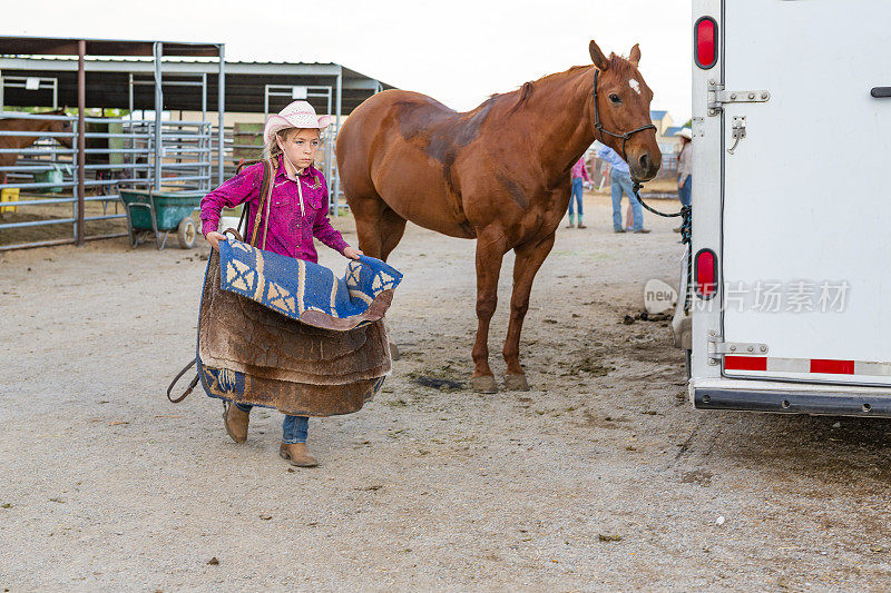 年轻的女牛仔在骑马后收起她的马鞍