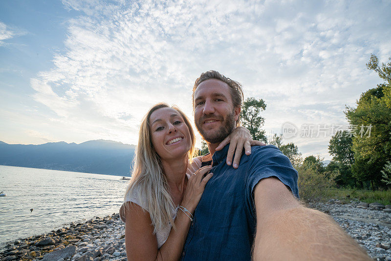 年轻夫妇在日落时分用移动设备在湖边自拍，瑞士