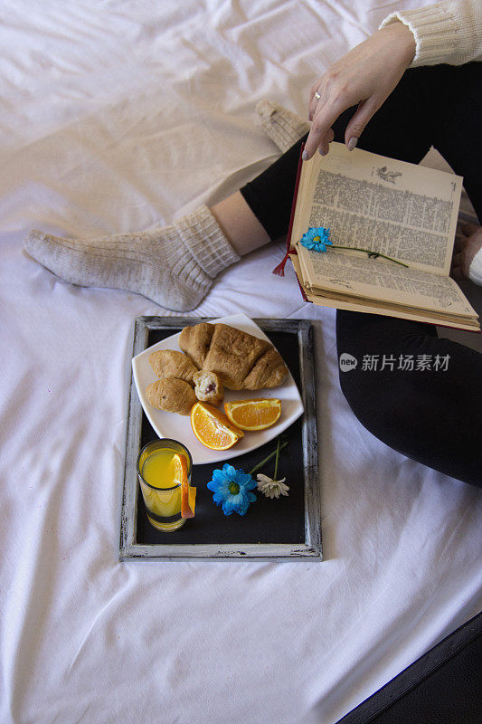 一个女人一边看书一边在床上吃早餐