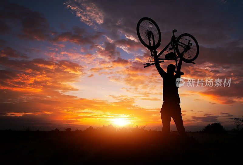 在夕阳西下的草地上，那个人把自行车举过头顶站着
