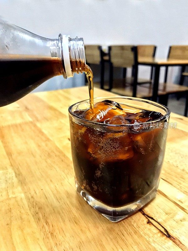 可乐在玻璃冰，把可乐从玻璃瓶饮料到一个有冰块的杯子，可乐在玻璃冰饮料在餐厅桌上饮料