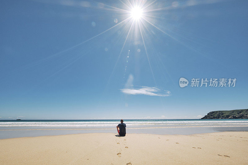 6月一个阳光明媚的炎热日子，康沃尔郡，一名男子坐在田园诗般的佩顿范德海滩的海岸线上。