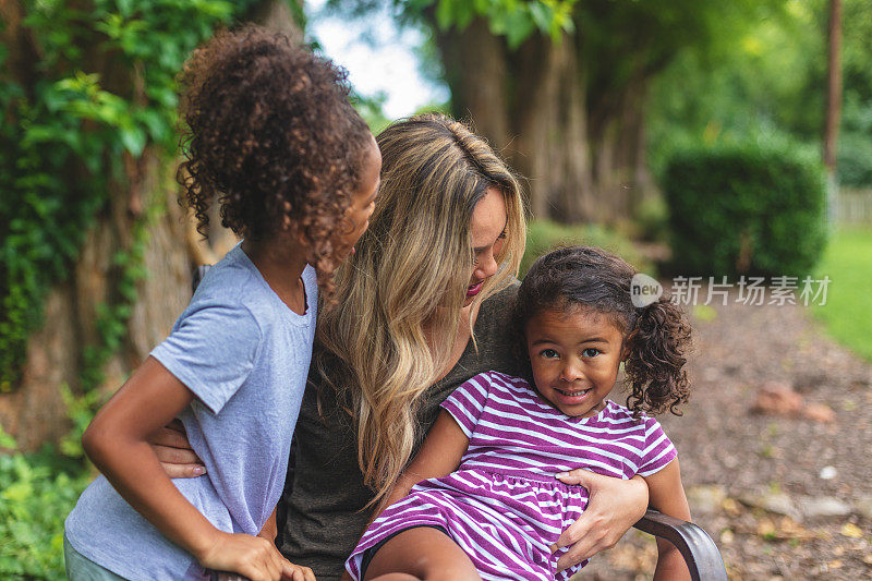 亚裔华人母亲和两个华裔和非裔美国人混血的女儿在一个绿色茂盛的后院里摆姿势拍照微笑和傻笑