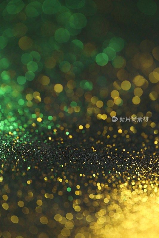壁纸手机闪闪发光。新年和圣诞节的背景。金色和绿色的闪光宏观背景与闪光的散景在黑色的背景。闪亮的纹理