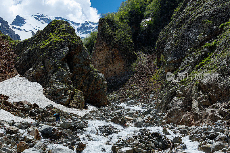 一个背包客穿过一条山间的河流，爬上了一座白雪覆盖的山顶