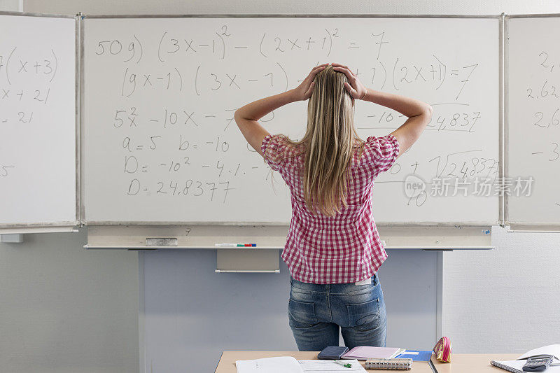 一个困惑和沉思的金发高中女孩手放在下巴站在白板前显示数学公式看板四分之三长度的镜头