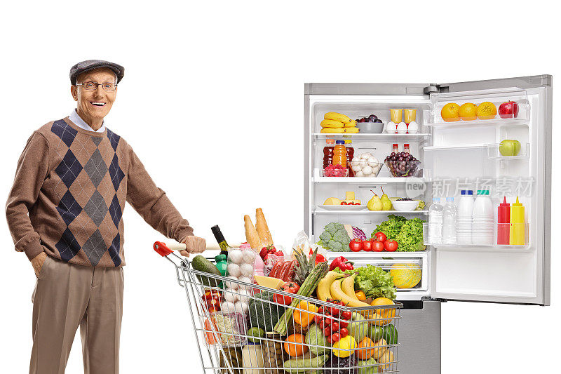 年迈的绅士推着装满食物的购物车站在冰箱前
