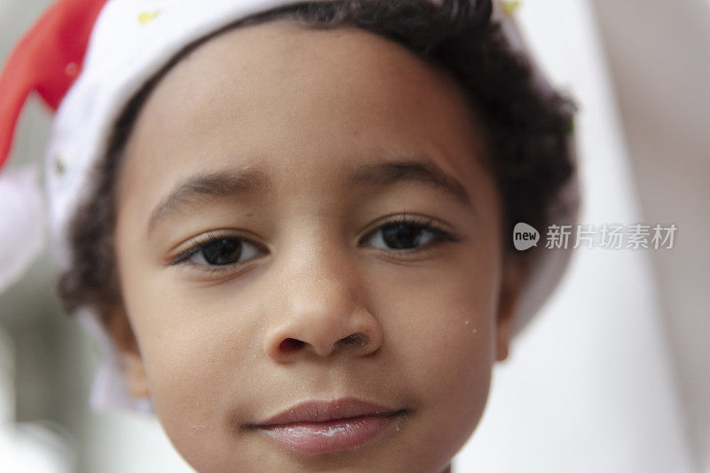 黑人小孩的肖像戴着圣诞帽和看着相机在圣诞节庆祝活动