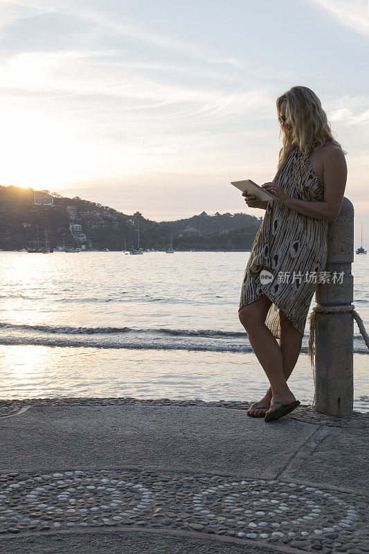 日出时分，一名女子在码头上使用平板电脑