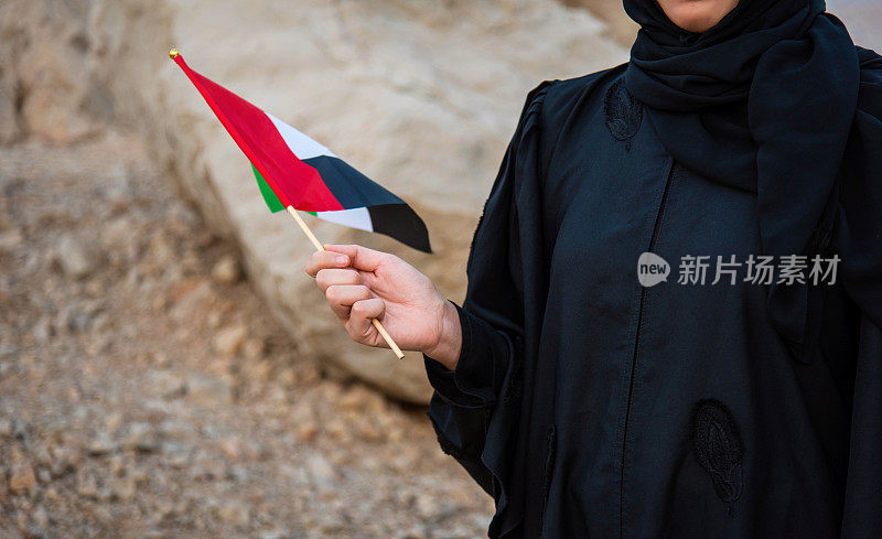 日落时分，一名阿联酋妇女在沙漠山区举着阿联酋国旗