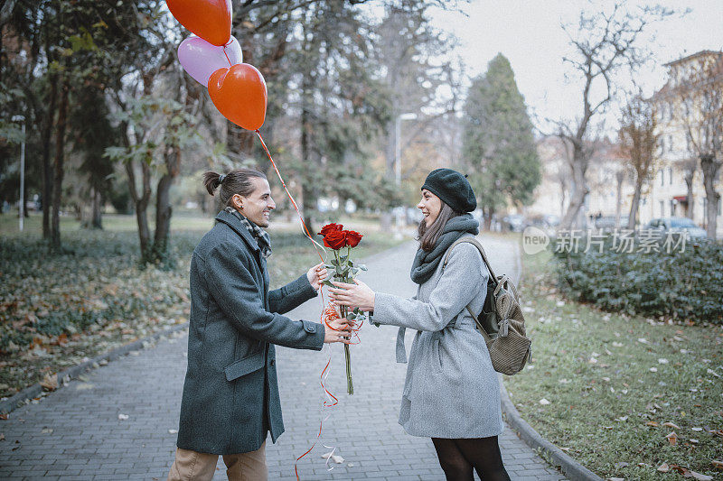 情人节这天，一名年轻男子将一束红玫瑰和心形气球送给女友。