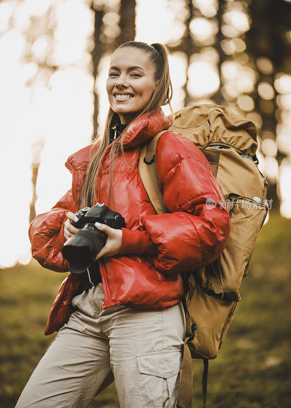 年轻的徒步旅行者与相机在自然界的肖像。成功的女人徒步登山在日出的山顶-年轻的女人背包上升到山顶。发现旅游目的地