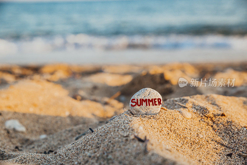 沙滩上的白色石头上刻着“夏天”