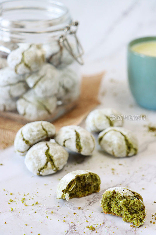 新鲜烘焙的抹茶苦杏仁饼干围绕着有盖的玻璃饼干罐，面包屑和碎饼干，大理石效果的背景，关注前景