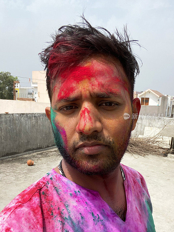 印度一名男子穿着库尔塔传统服装，身上涂满了油漆粉，在胡里节的色彩和爱漆大战中胡闹，微笑着看着镜头