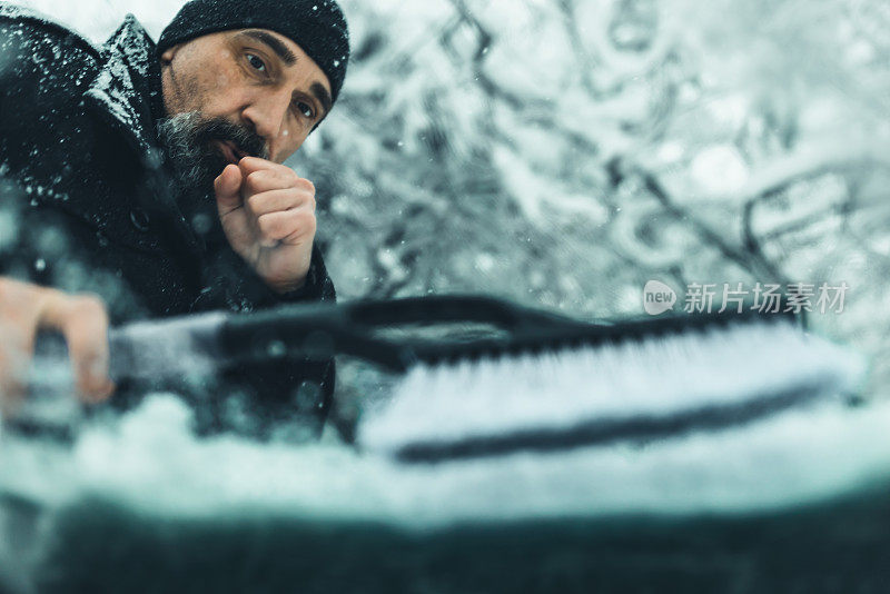 汽车的冬季问题。一个人用刷子清理汽车上的积雪