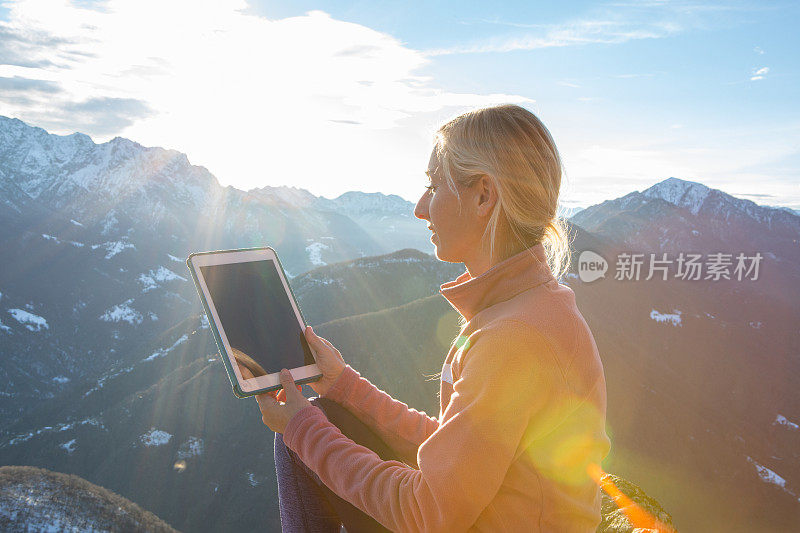年轻的徒步旅行者在日出时坐在山顶上使用数码平板电脑