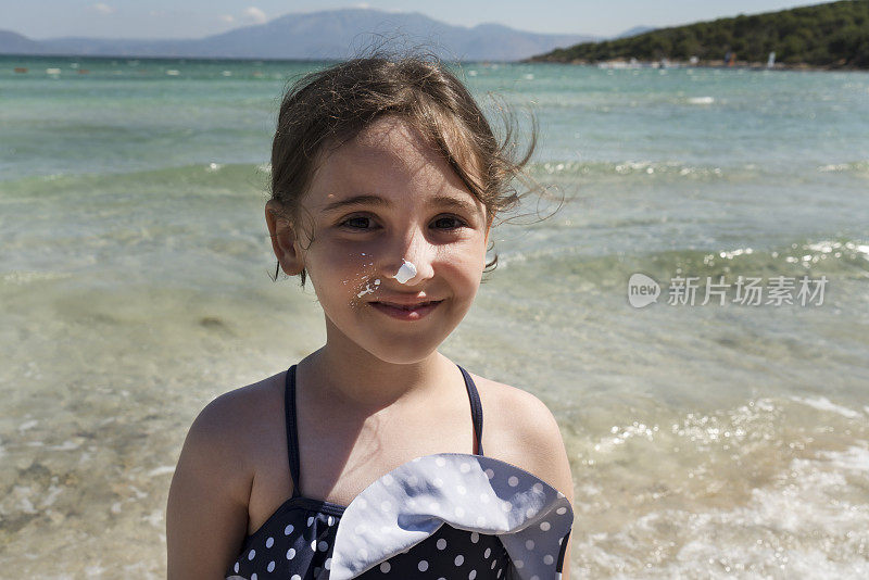 一个微笑的小女孩的肖像，脸上涂着防晒霜
